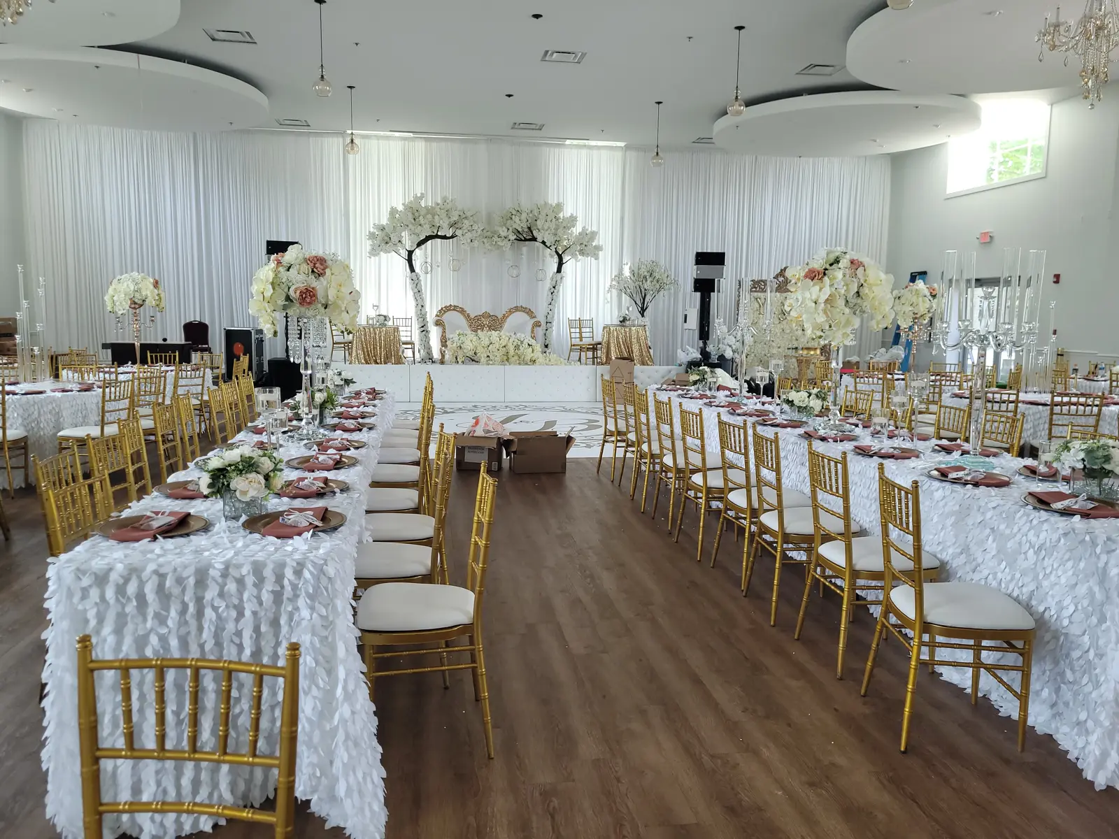 Long banquet tables with white ruffled linens, gold chiavari chairs, and elaborate floral arrangements