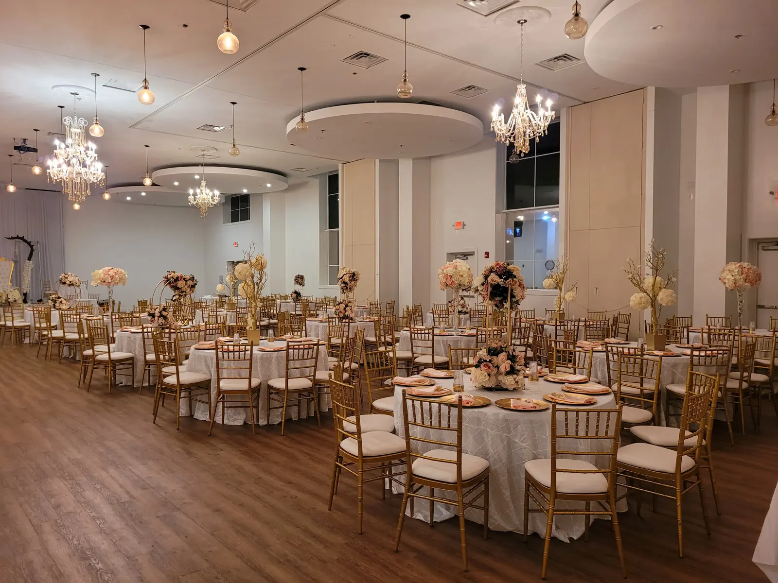 Wide evening view of the hall with round tables, floral centerpieces, and warm chandelier lighting