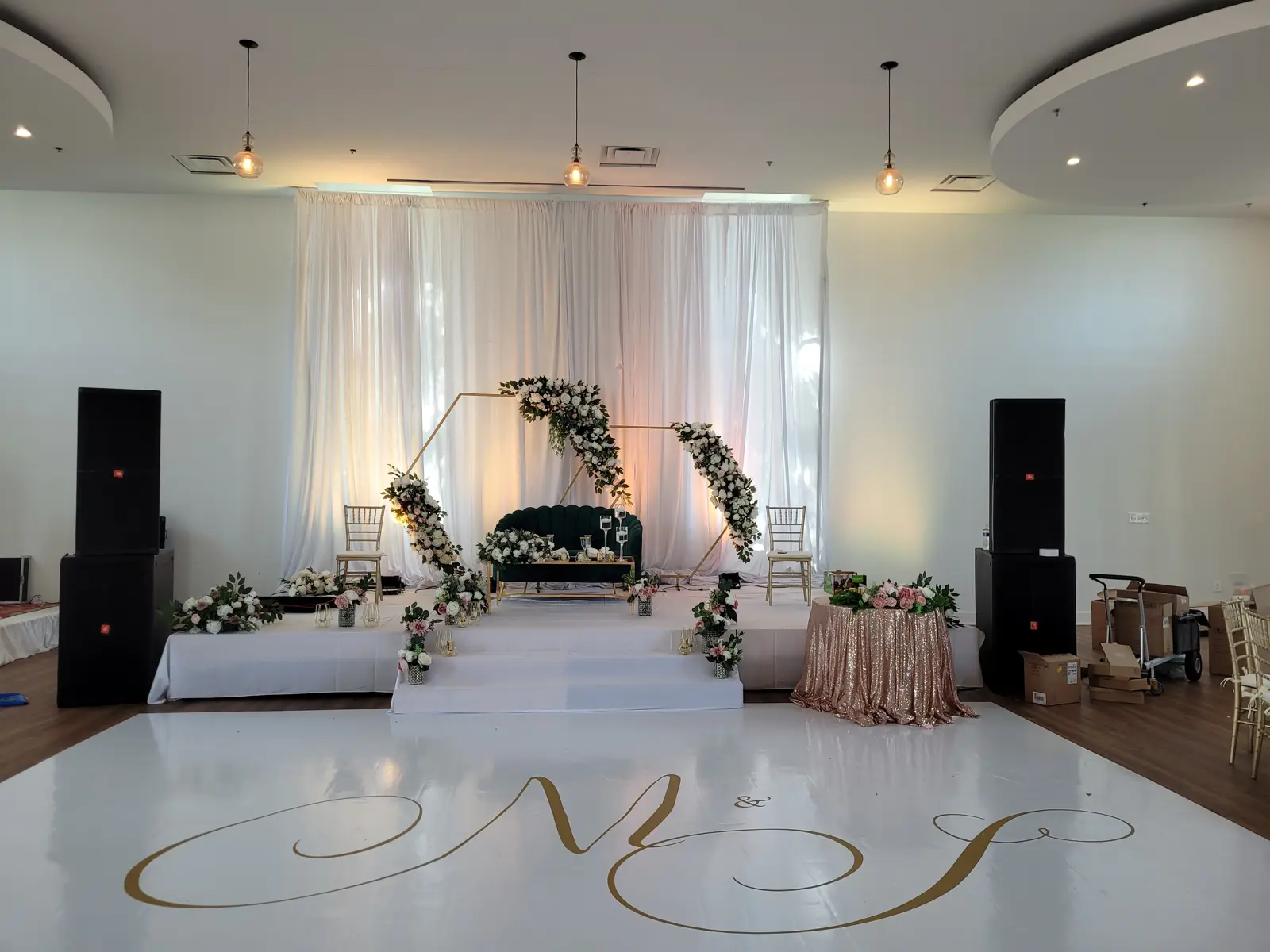 Wedding stage with floral arch, monogrammed dance floor, and speakers
