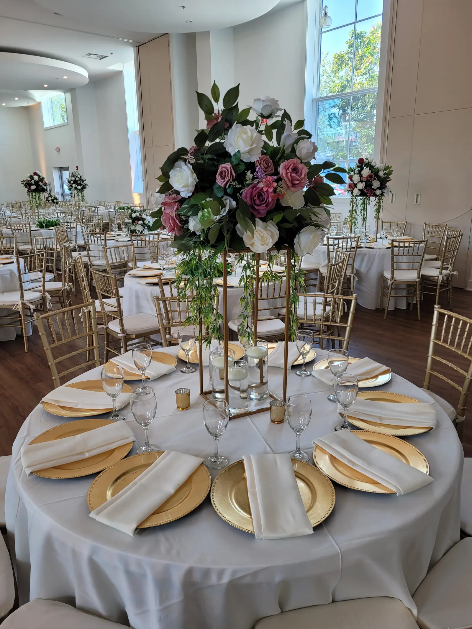 Close-up of elegant table setting with gold charger plates, crystal glasses, and tall floral centerpiece