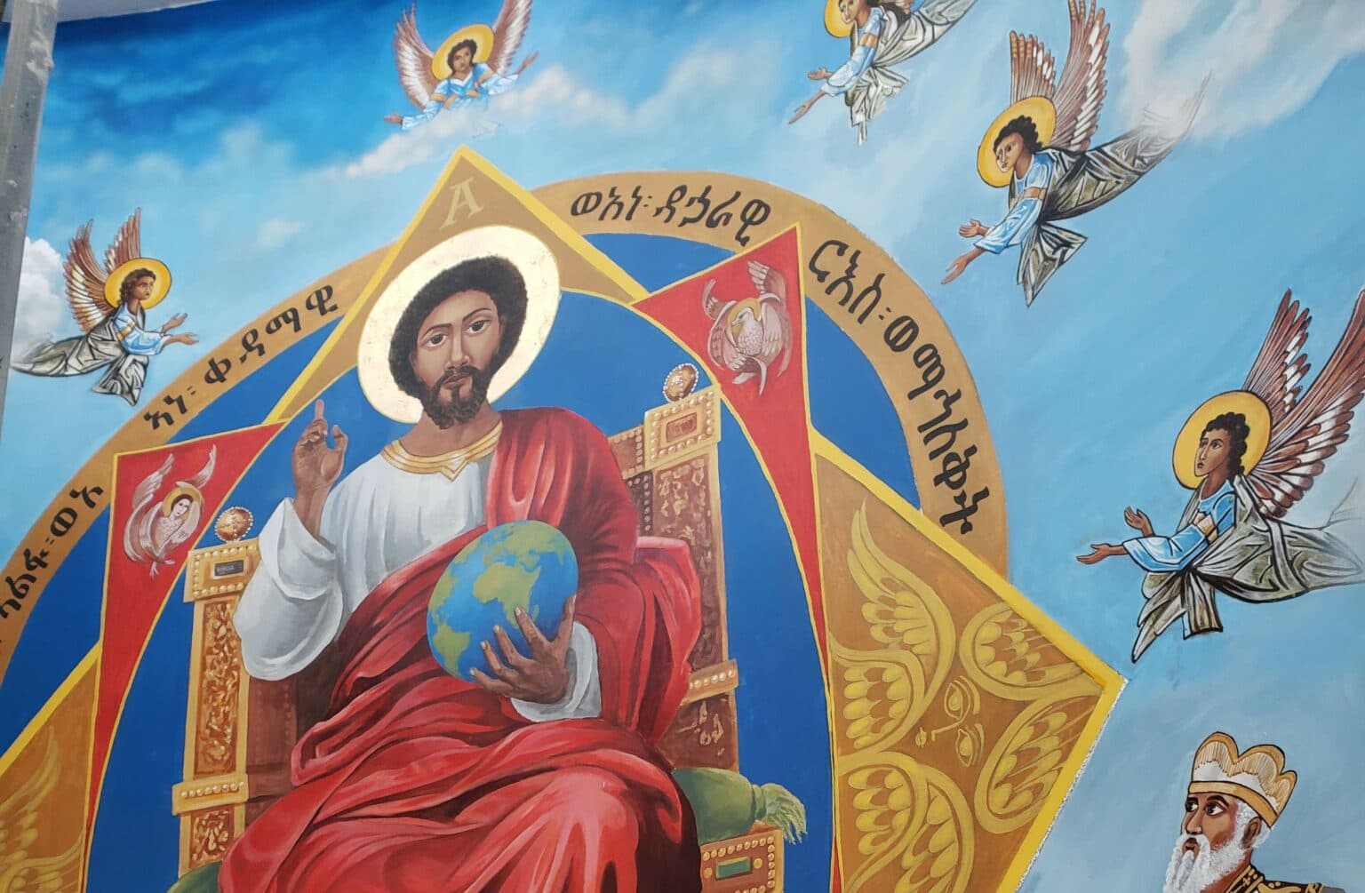 Orthodox mural of Christ enthroned holding the globe, surrounded by angels with gold halos and Ge'ez scripture