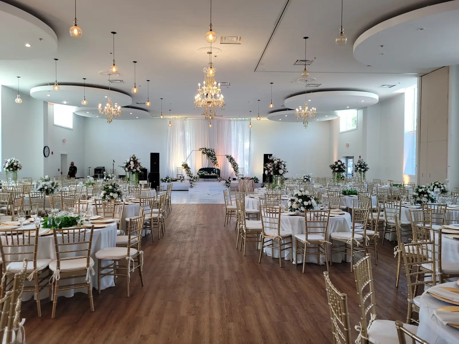 Medhane Alem hall set for a wedding reception with round tables, gold chiavari chairs, and crystal chandeliers